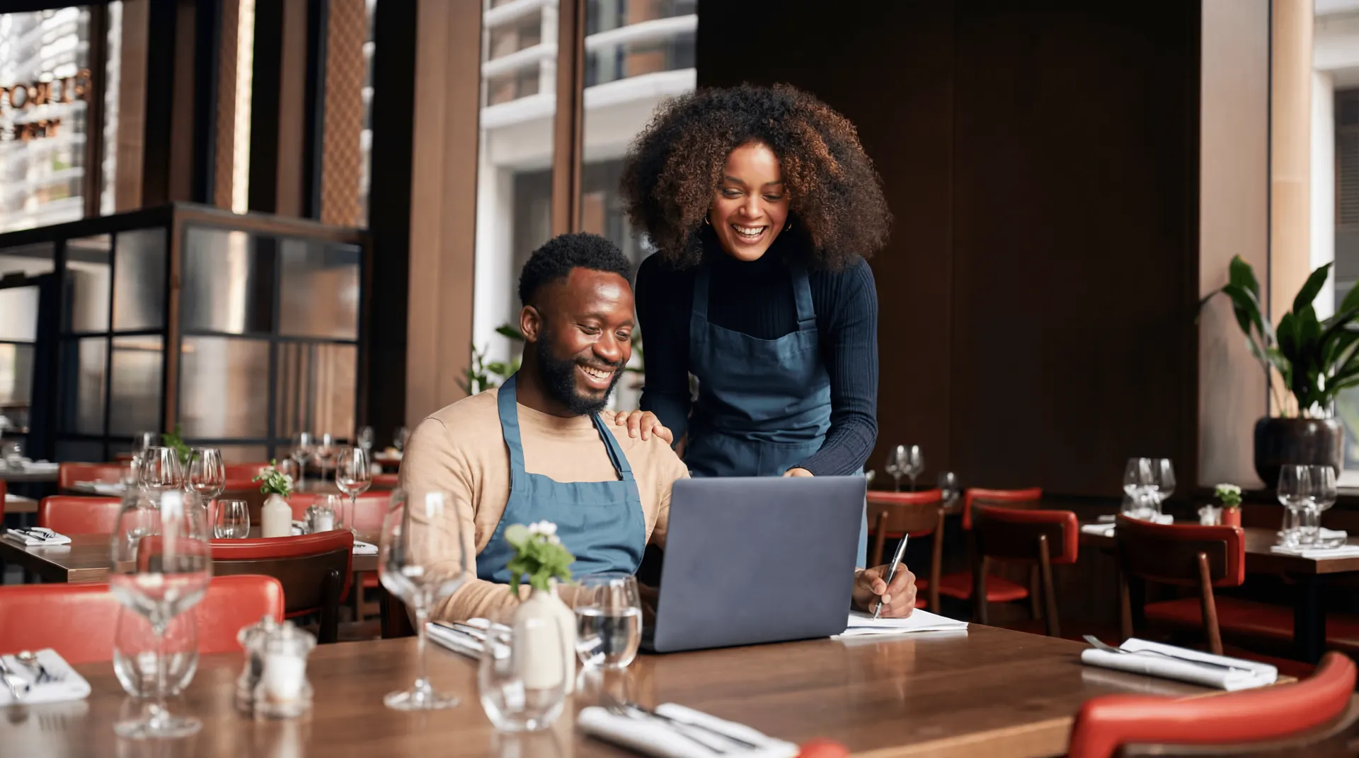 Two restaurant owners smiling while registering their restaurant on a laptop in their dining room