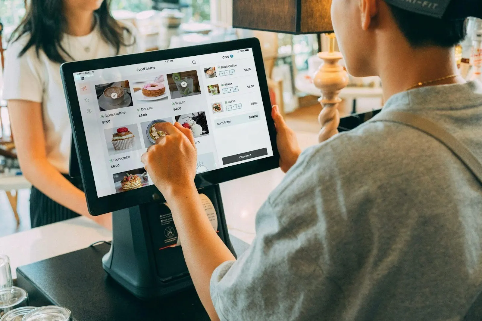 Staff member using a self-order kiosk screen to ring up a customer's coffee shop order