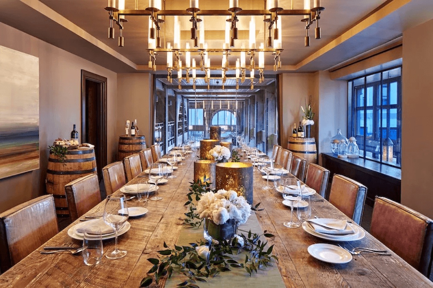 Elegant private dining room with a long wooden table set for a group event, wine barrels, flower centerpieces, and a statement chandelier